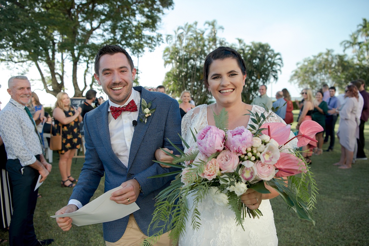 Happy bride and groom following wedding ceremony at Mindel Beach lawns, bride carries Beija Flor bouquet of fragrant peonies.