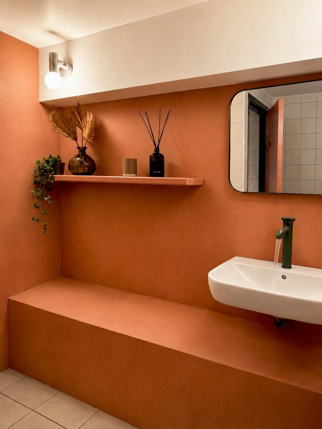 Men's restroom entrance: Nazka Restaurant men's washroom entrance showcasing troweled terracotta-colored walls, a rectangular mirror, and a white basin with a distinctive stepped platform below, designed by Studio Michiel Wijnen.