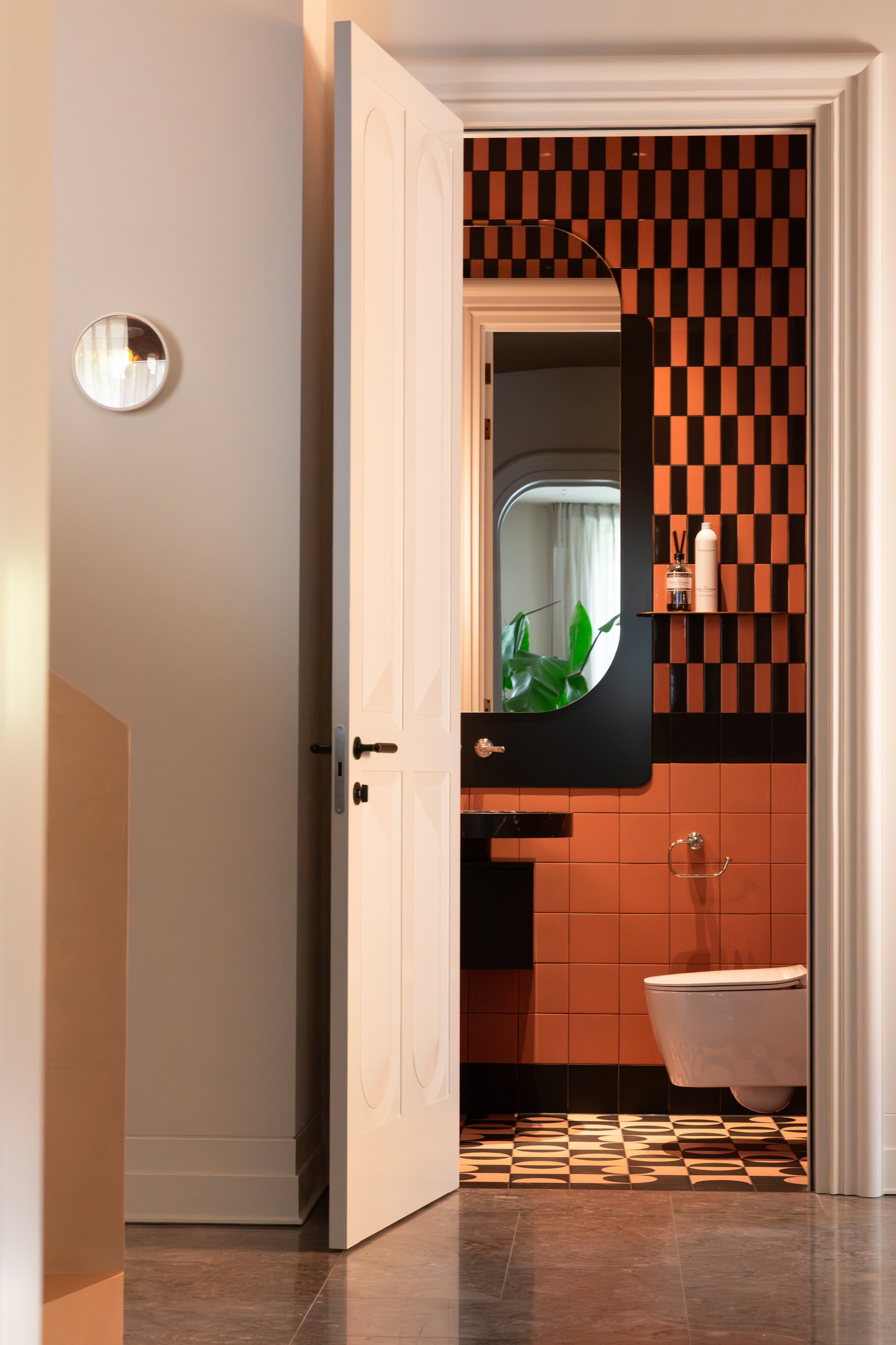 14. Orange and black bathroom threshold: View of the contrasting orange and black Quintessenza Argblock patterned bathroom, featuring a black accent surface, custom door, and DND hardware.