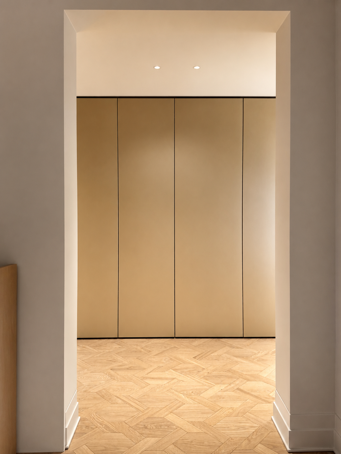 2. Gold wardrobe & lighting: View of a gold-finished custom wardrobe framed by a square passage, illuminated by minimalist recessed Prado spotlights.
