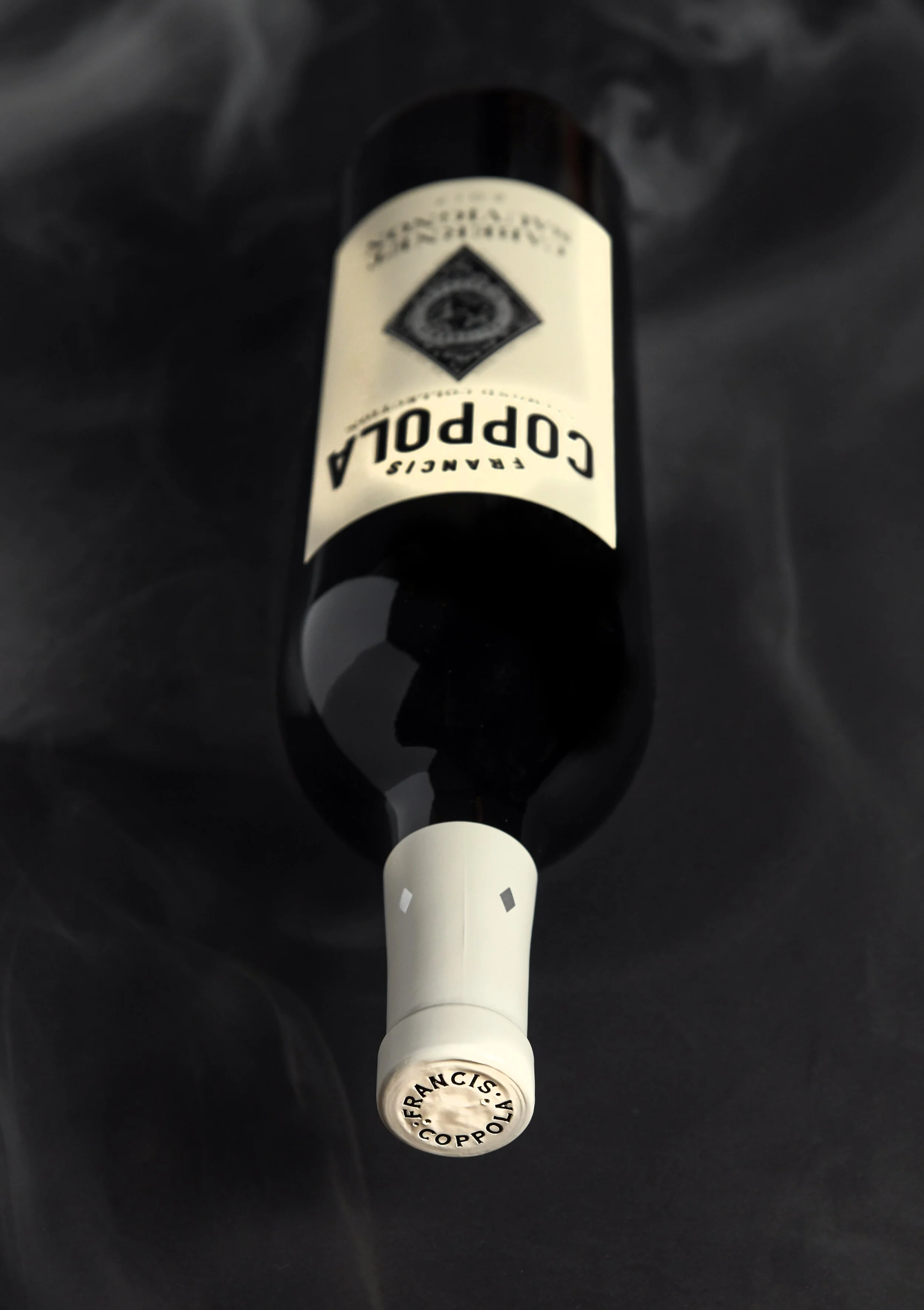 A wine bottle with a white label and a white capsule on the neck, placed on a black surface, with the label reading "Coppola" and the capsule marked with "Francis Coppola."