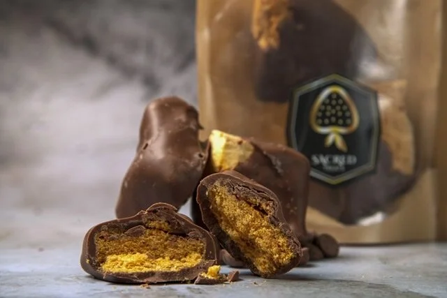 Close-up of chocolate candy with a yellow filling, some pieces are broken open, with a package of similar chocolates in the background.