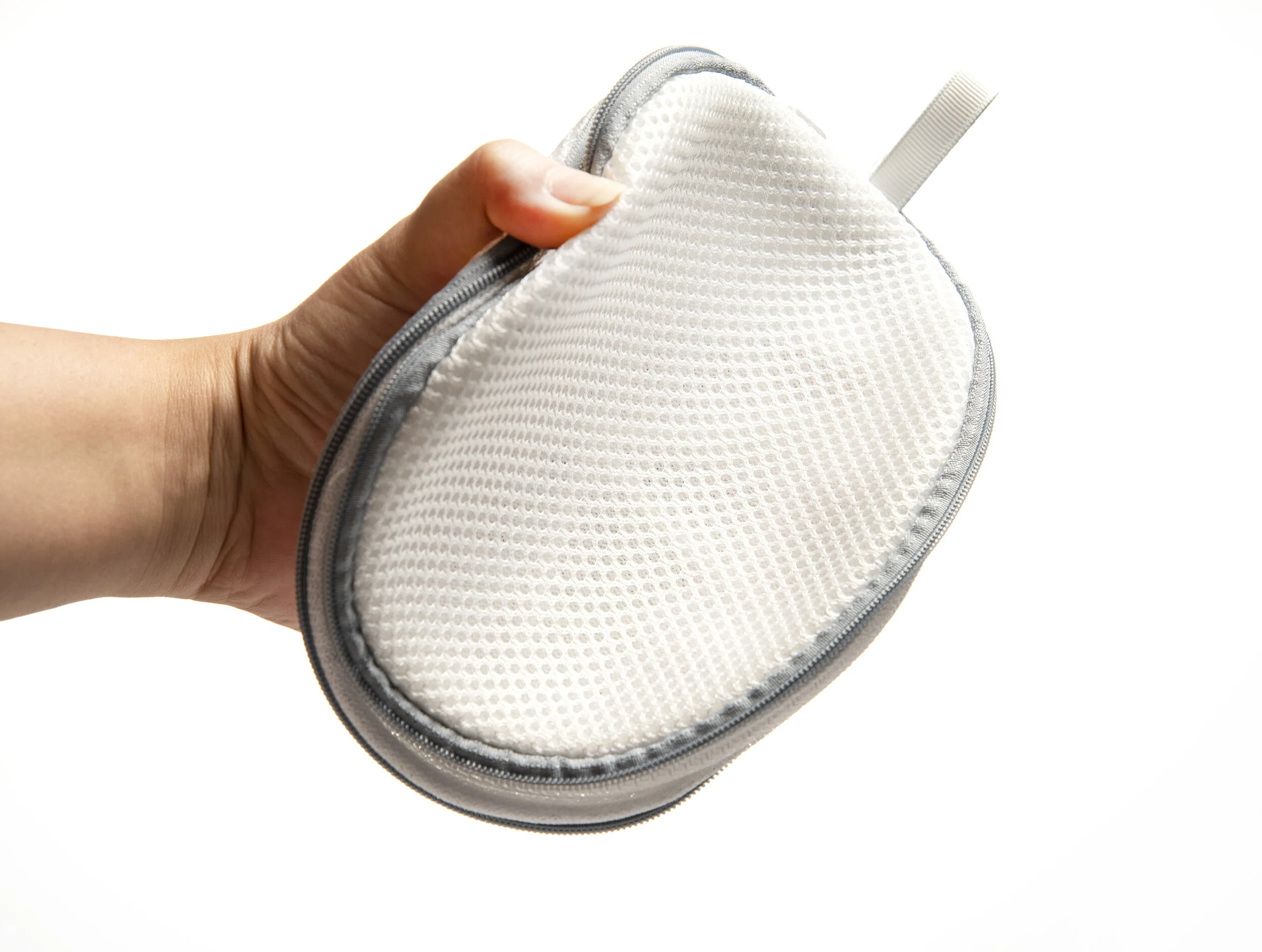 A hand holding a round, white, textured cloth case with a zipper, against a plain white background.