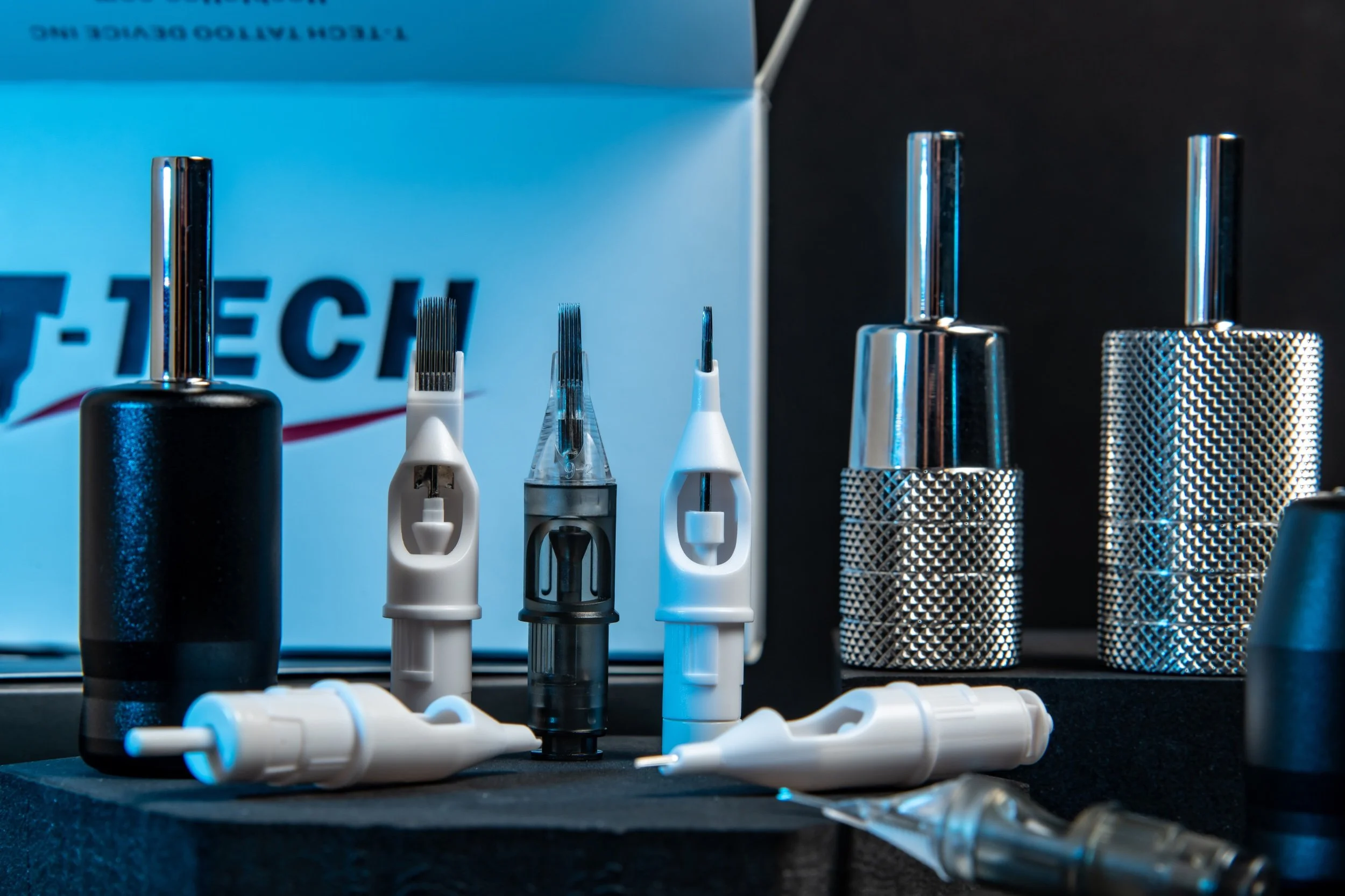 Tattoo machine parts and needles displayed on a table with a blue background.