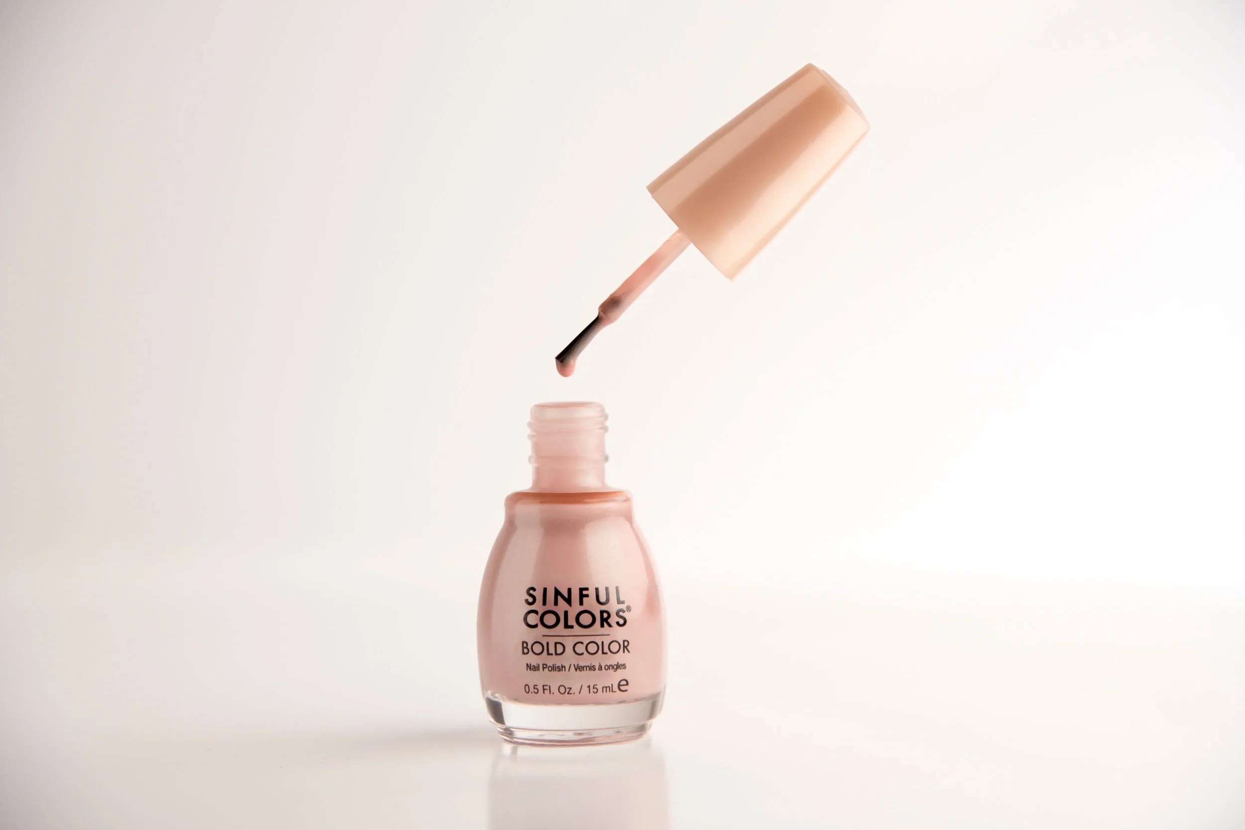 Pink nail polish bottle labeled "Sinful Colors Bold Color" with the cap removed and the brush lifted above the bottle, against a white background.