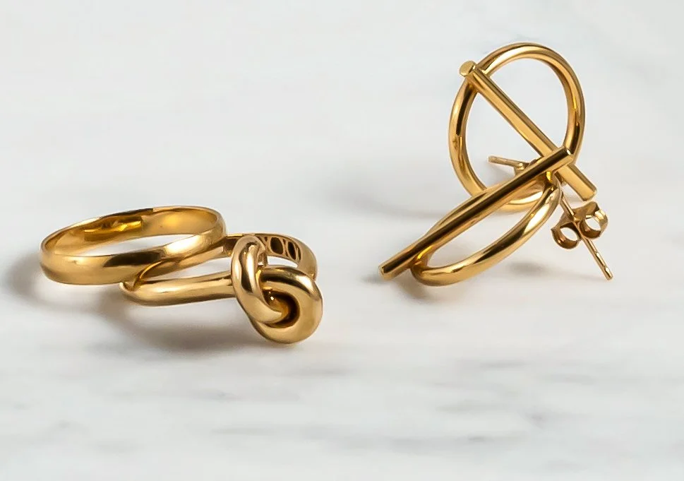 Two pairs of gold hoop earrings with knot and bar designs placed on a white surface.