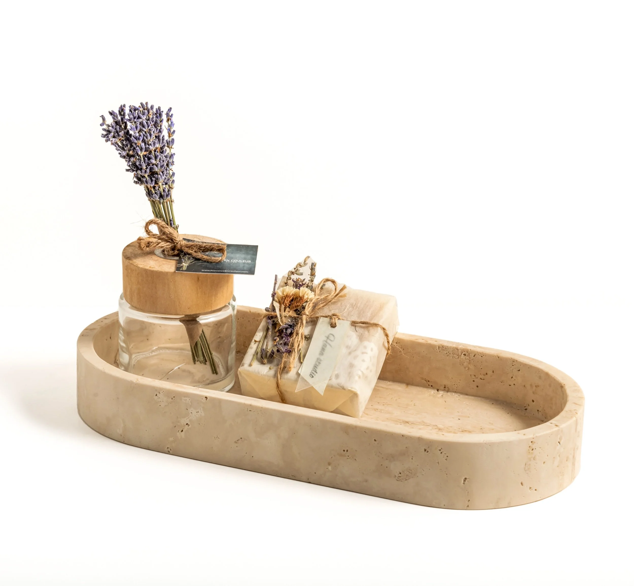 A beige marble tray with a small glass jar with a wooden lid containing lavender flowers, a wrapped soap or package tied with twine and lavender, on a white background.
