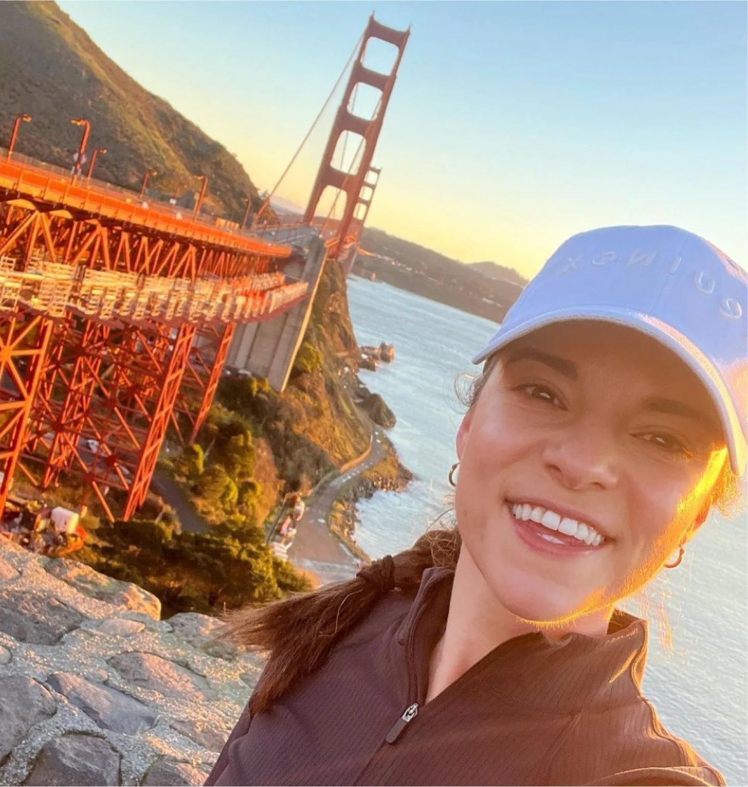 A person taking a selfie near the Golden Gate Bridge during sunset.