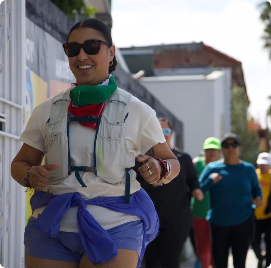 People jogging in outdoor setting, wearing athletic gear and sunglasses, with a woman in front smiling.