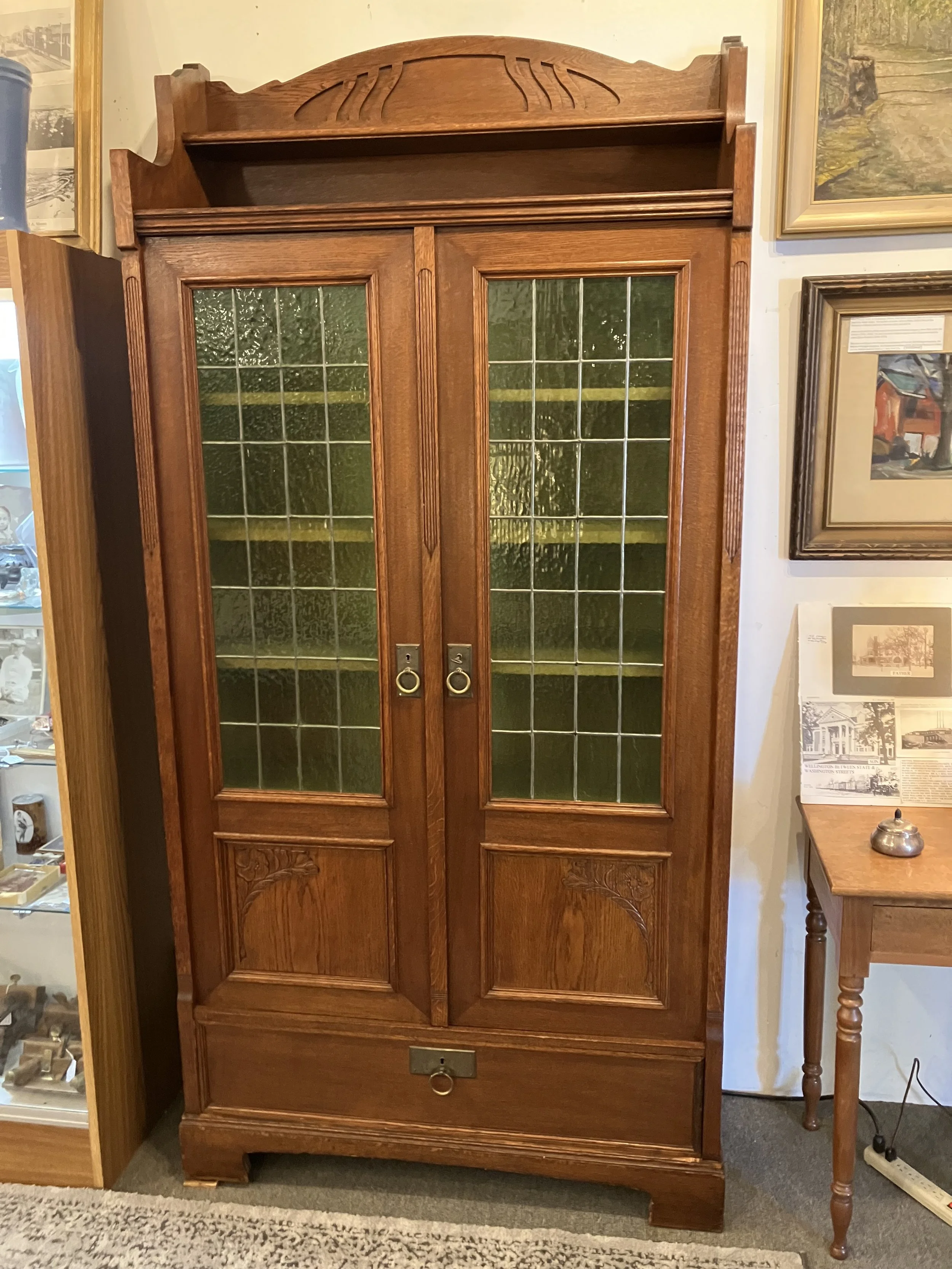  2261037 Belgian, Oak, Bookcase. Two doors with leaded glass and Art Nouveau carved panels. One drawer. Circa 1900. 42” W x 16”D x 87” H.  