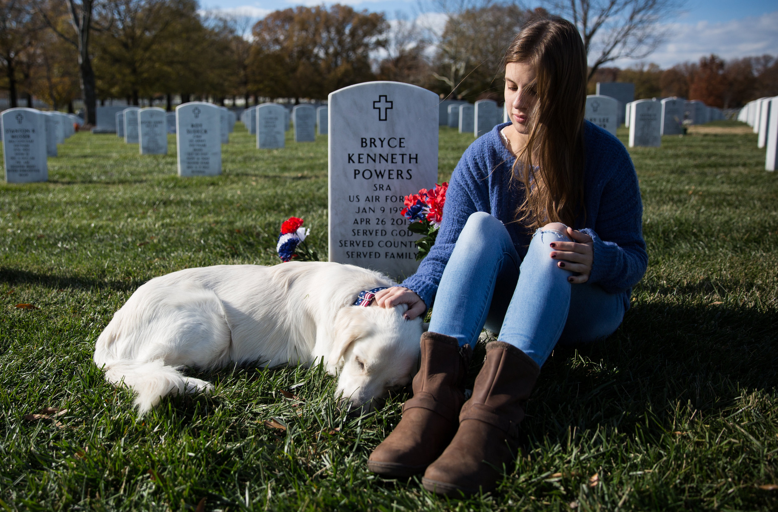 Madi Powers sits near the grave of her brother, Senior Airman Bryce Powers at Arlington National Cemetery. SRA Powers died in 2013 as the result of a car crash during his deployment in Japan. The dog is a service dog named after her broth