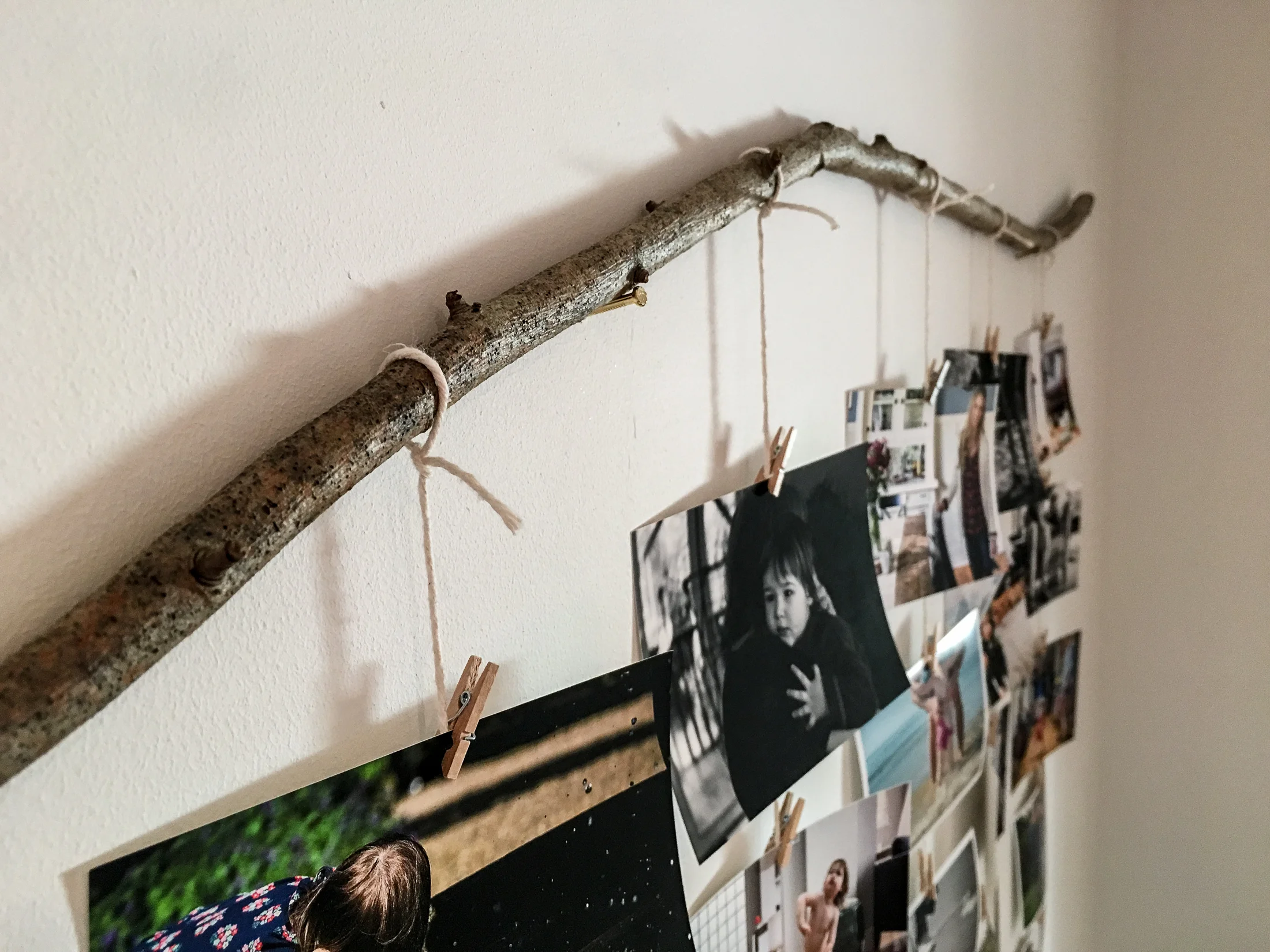 Detail of twine attached to stick with mini clothespins holding small photographs.