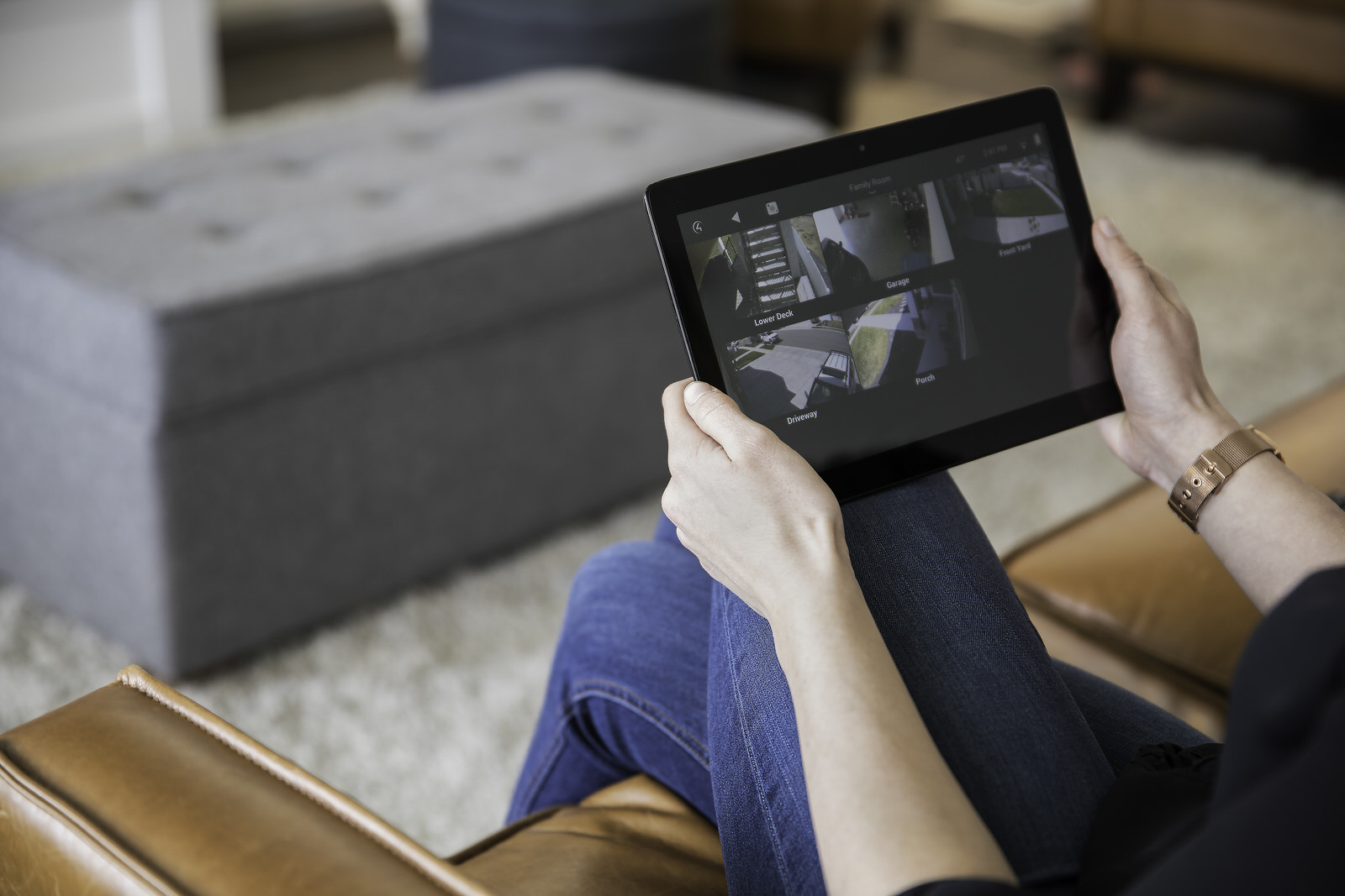 Smart_Home_Security_Man_Sitting_On_Brown_Sofa_Holding_iPad_Watching_Video_CCTV_Camera_Surveillance_Blue_Jeans_Grey_Rug