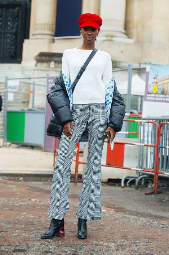 Model Tami Williams wears a red newsboy cap and a black adidas bomber jacket over a white sweater with grey houndstooth trousers, outside the Chanel show via Refinery29 