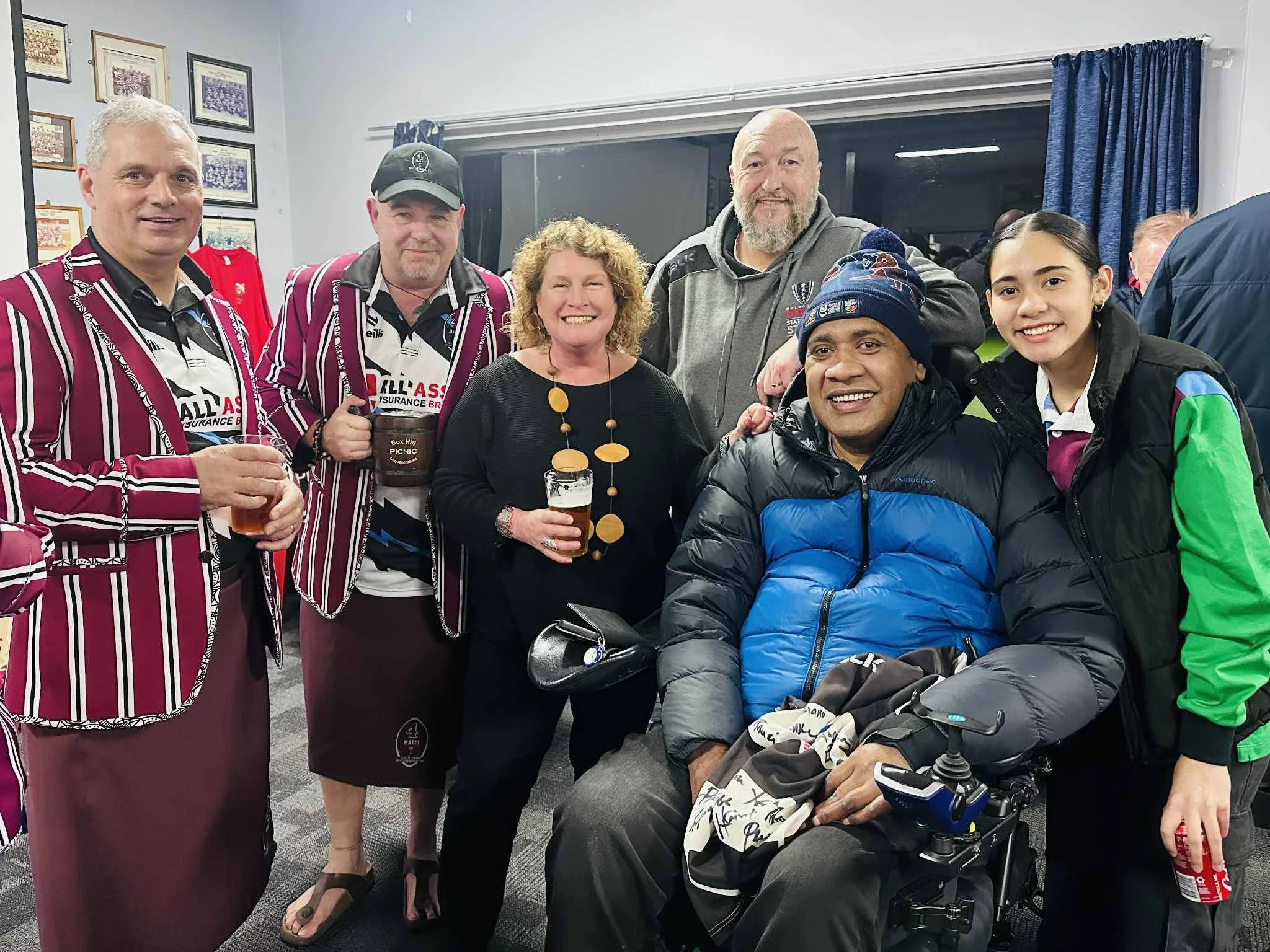 Group of people at a social gathering, some wearing striped blazers and holding drinks, others smiling for the camera.