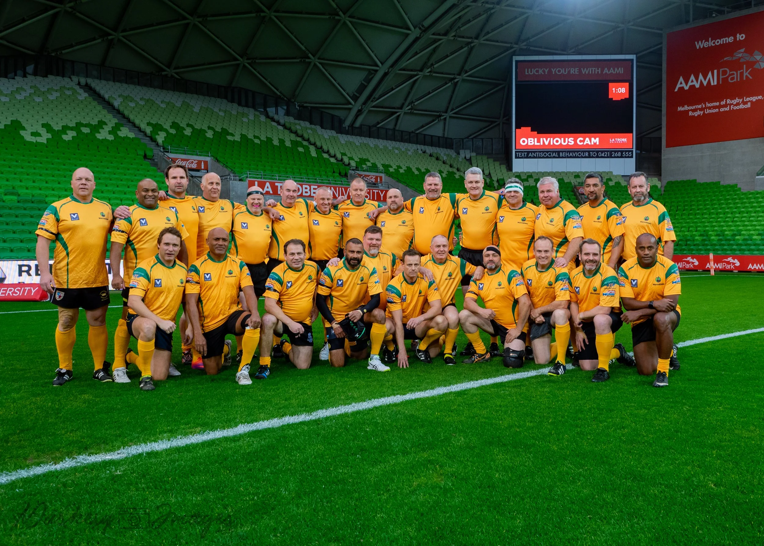 Group of rugby players in yellow jerseys posing on a rugby field inside a stadium.