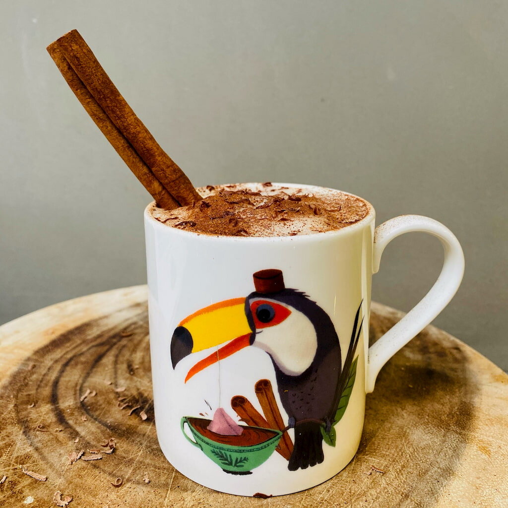 Frothy Happy Toucan drink with oat milk and cinnamon stick in toucan mug on rustic board