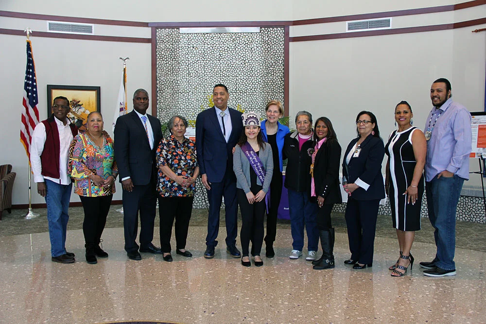 Senator Elizabeth Warren (center, in blue jacket), poses with members of the Wampanoag Tribe during her visit to the Wampanoag Health Unit on April 21. Pictured from left to right are: Medicine Man Earl (Soaring Eagle) Cash Jr.; Ann Marie Askew; tribe treasurer Gordon Harris; tribal councilwoman Yvonne Avant; Mashpee Wampanoag Tribal Council chairman Cedric Cromwell; Chenoa Peters; Senator Warren; Pauline Peters; Winnie Johnson-Graham; Rita Consalvos; Cheryl Frye-Cromwell; and Brian Weeden.