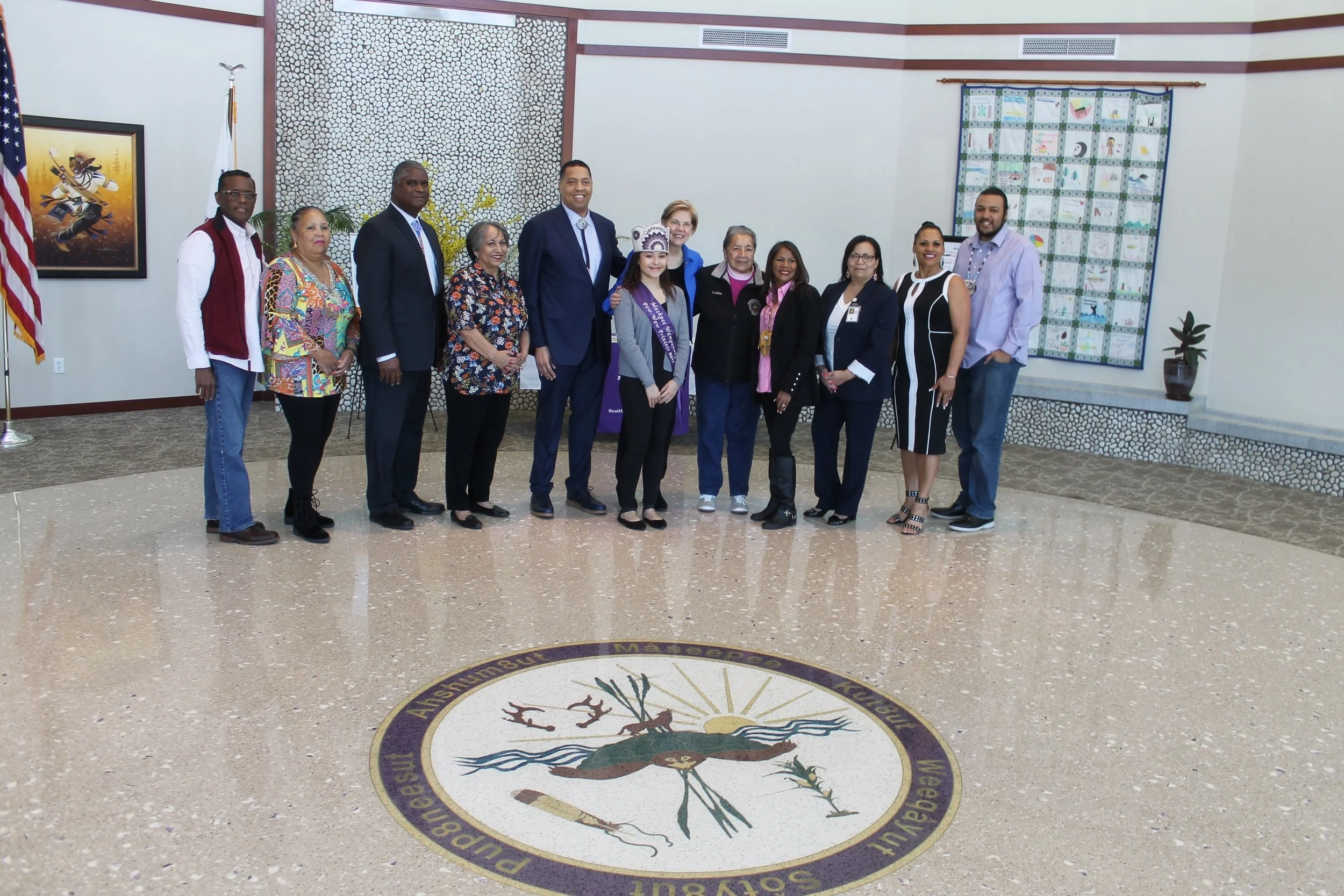 Senator Elizabeth Warren (center, in blue jacket), poses with members of the Wampanoag Tribe during her visit to the Wampanoag Health Unit on April 21. Pictured from left to right are: Medicine Man Earl (Soaring Eagle) Cash Jr.; Ann Marie Askew; tribe treasurer Gordon Harris; tribal councilwoman Yvonne Avant; Mashpee Wampanoag Tribal Council chairman Cedric Cromwell; Chenoa Peters; Senator Warren; Pauline Peters; Winnie Johnson-Graham; Rita Consalvos; Cheryl Frye-Cromwell; and Brian Weeden.