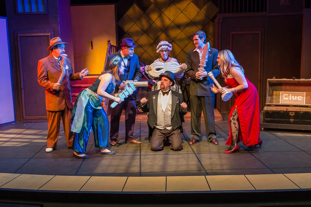 Six murder suspects, each holding a possible murder weapon, surround Mr. Boddy (Mike Owens) in a scene from Waukesha Civic Theatre's "Clue: The Musical." Pictured, from left, are Colonel Mustard (David Jirik), Mrs. Peacock (Margaret Teshner), Professor Plum (Andrew Byshenk), Mrs. White (Laura Heise), Mr. Green (Thomas Hess) and Miss Scarlet (Rachel Krause).