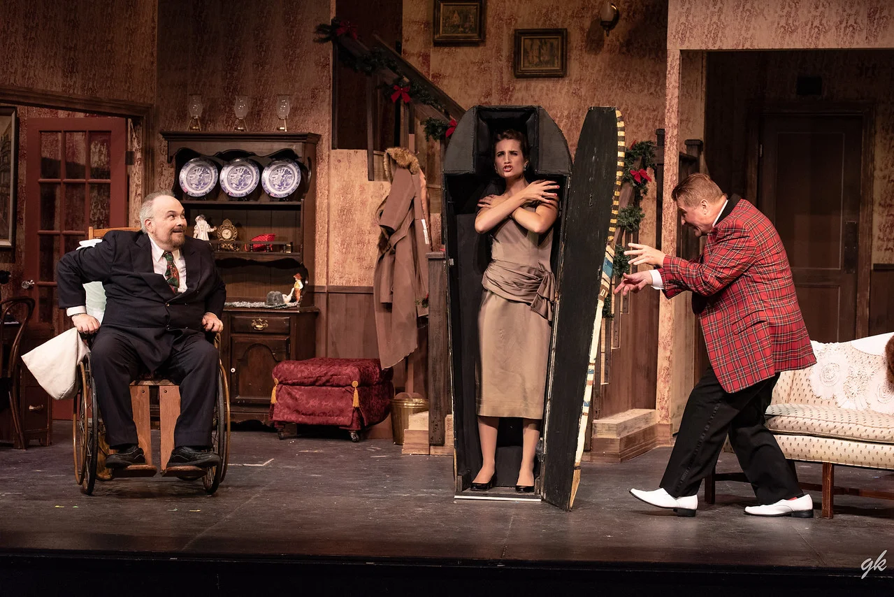 Actress Lorraine Sheldon (Kat Zilka) creates a dramatic moment as she gets into a gift Egyptian sarcophagus delivered to Sheridan Whiteside (Hal Erickson), left, while Sheridan's friend Banjo (Jim Stahl) gets ready to close it up in a scene from Sunset Playhouse's "The Man Who Came to Dinner."