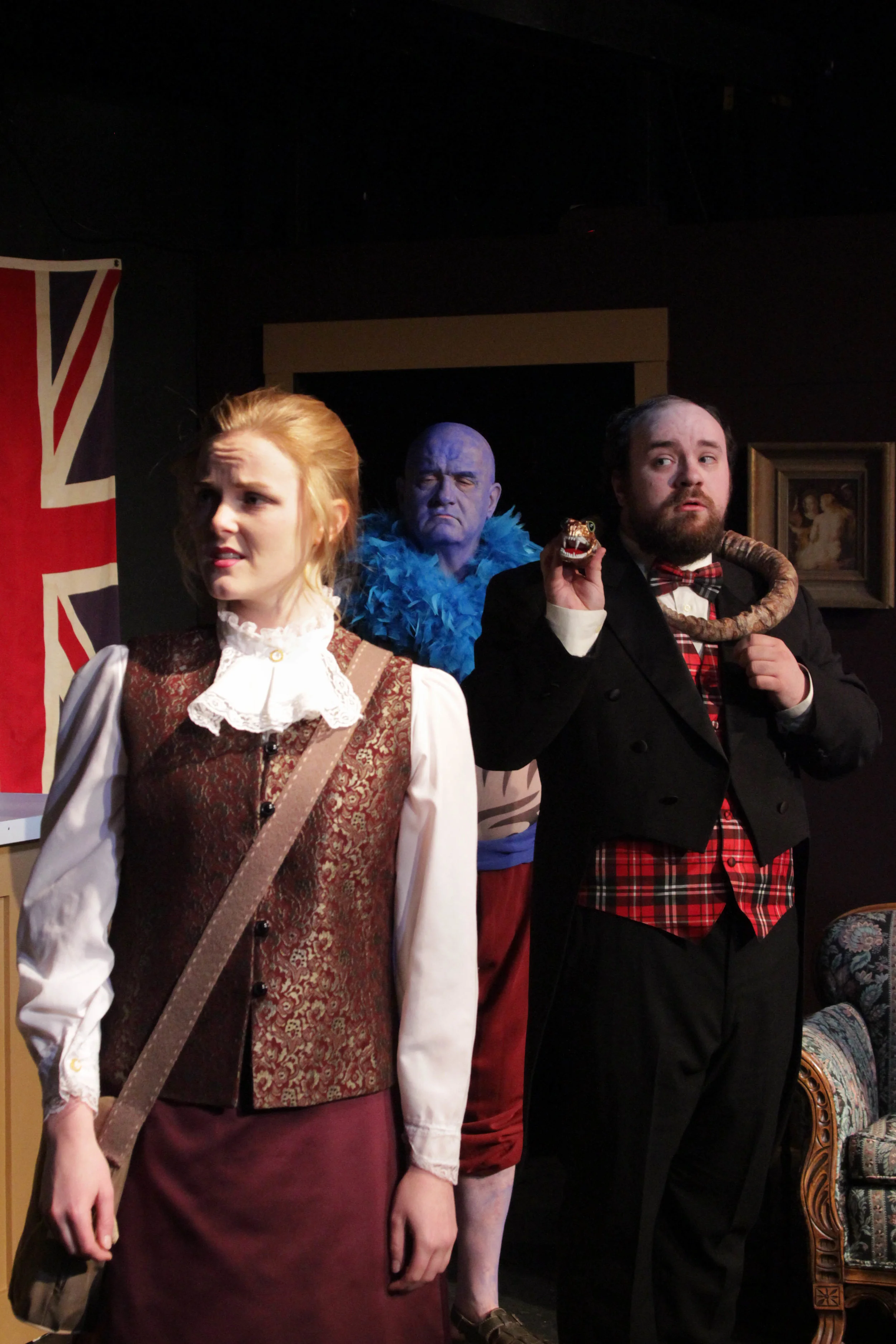 Professor Cope (Logan Milway), wearing his beloved snake Rosie, listens to prospective Explorers Club member Phylida (Katie Krueger) along with a member of a long-lost tribe (Mike Crowley) she has brought to a meeting.