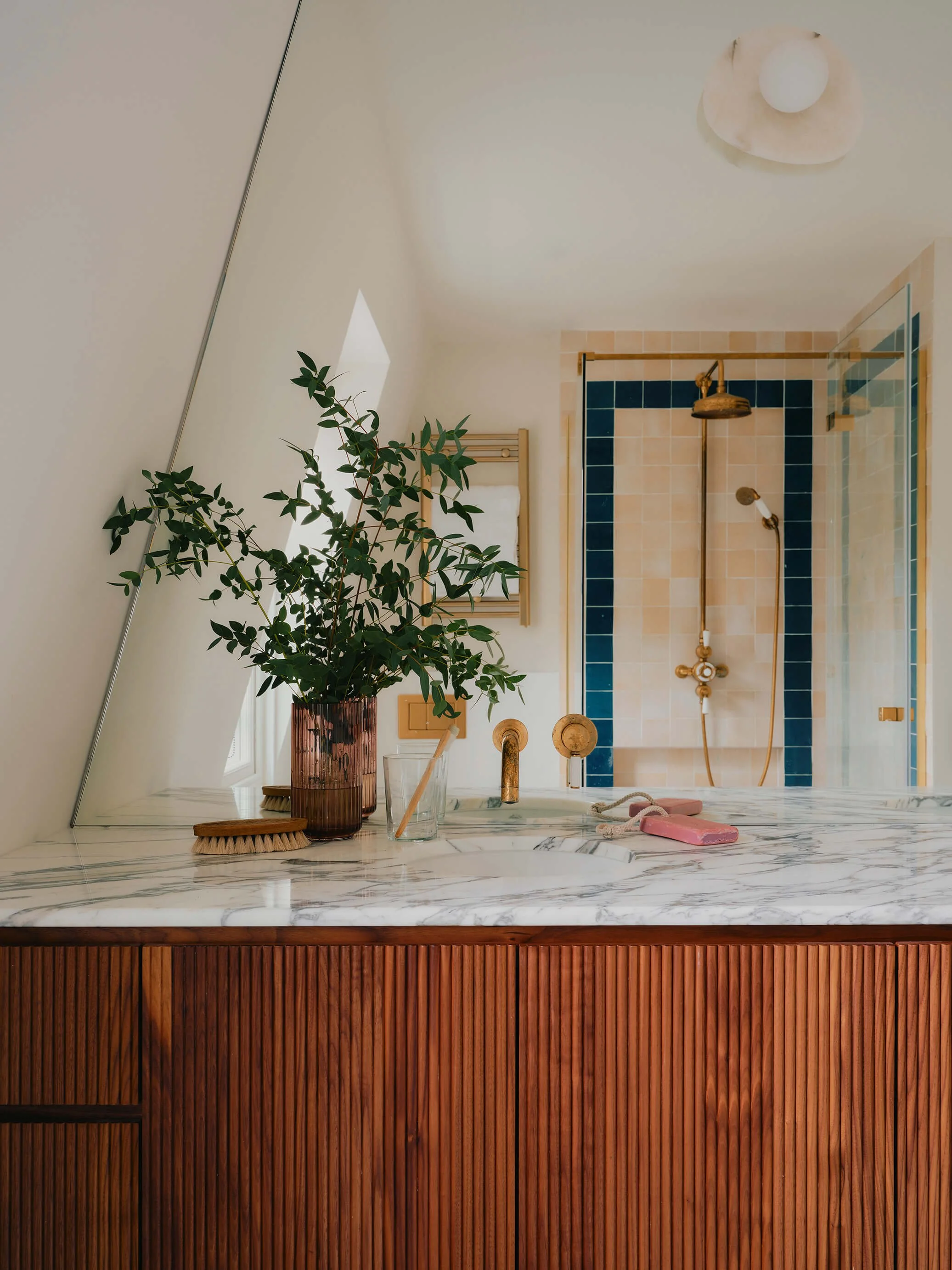 Marble, wood, and tiled bathroom with green plant in vase next to the sink