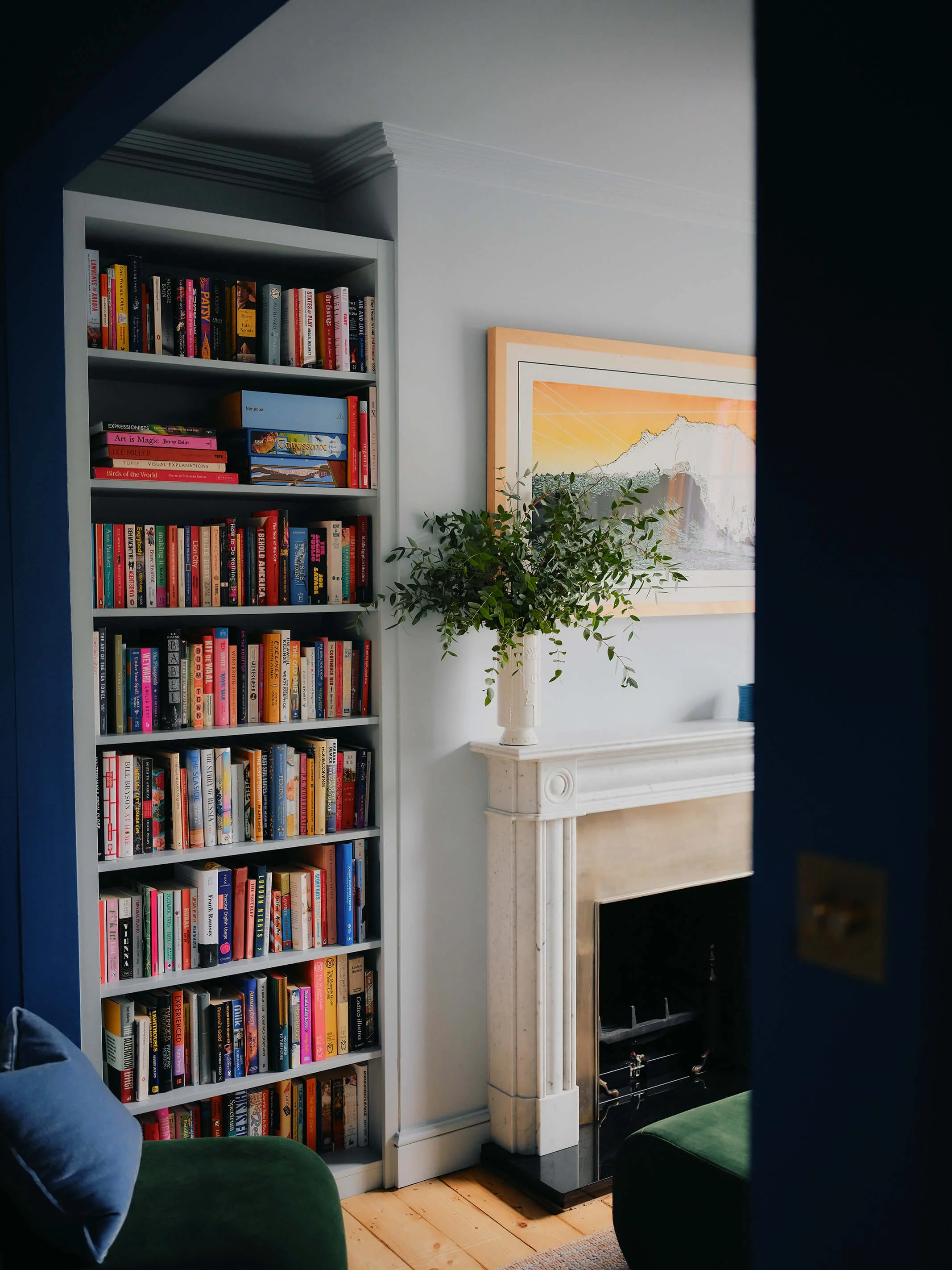 Pale blue livingroom with fireplace, wooden floors, and filled colourful bookcase.