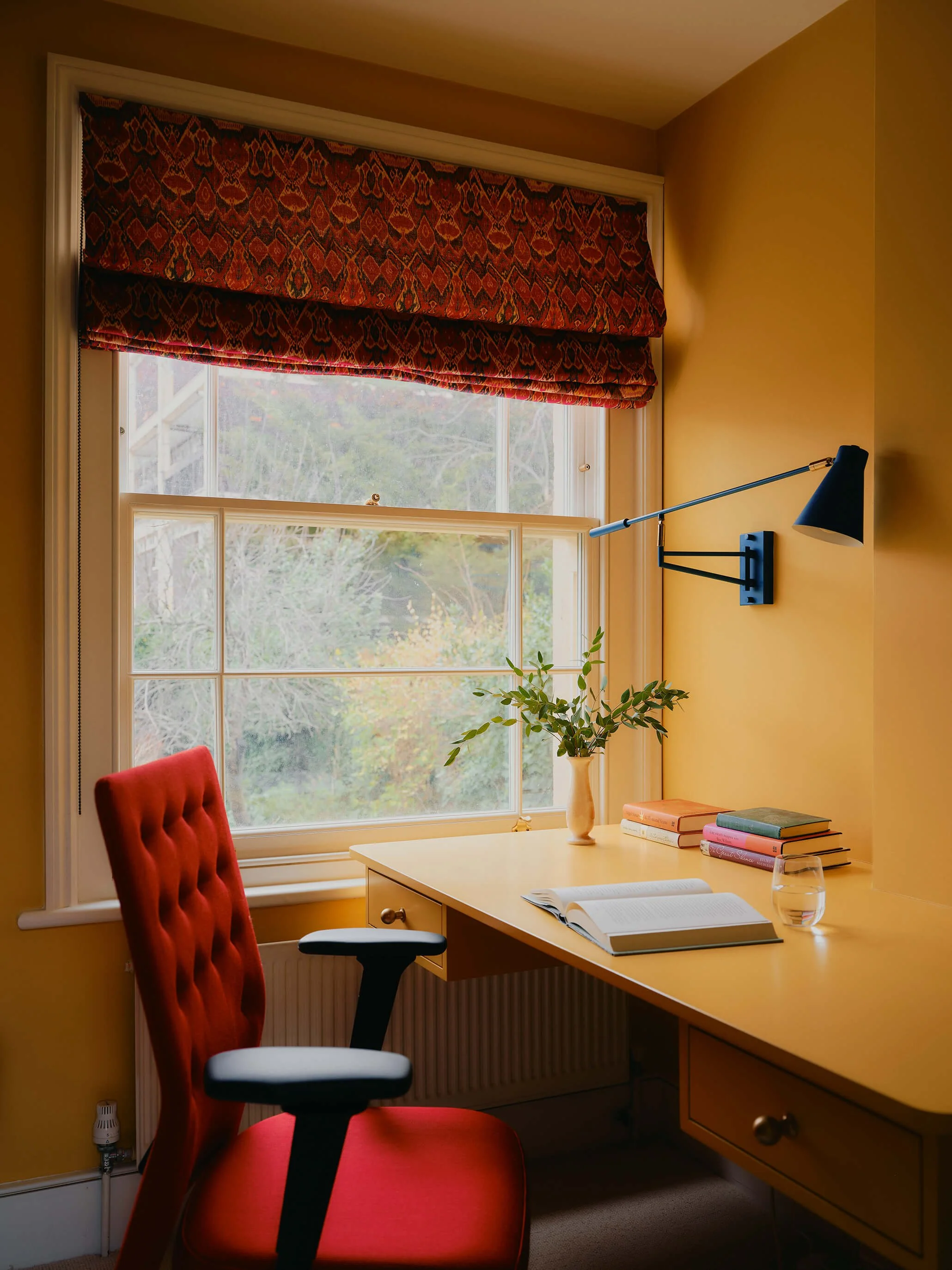 Bright yellow desk space, with desk next to window, bright red office chair tucked into desk.