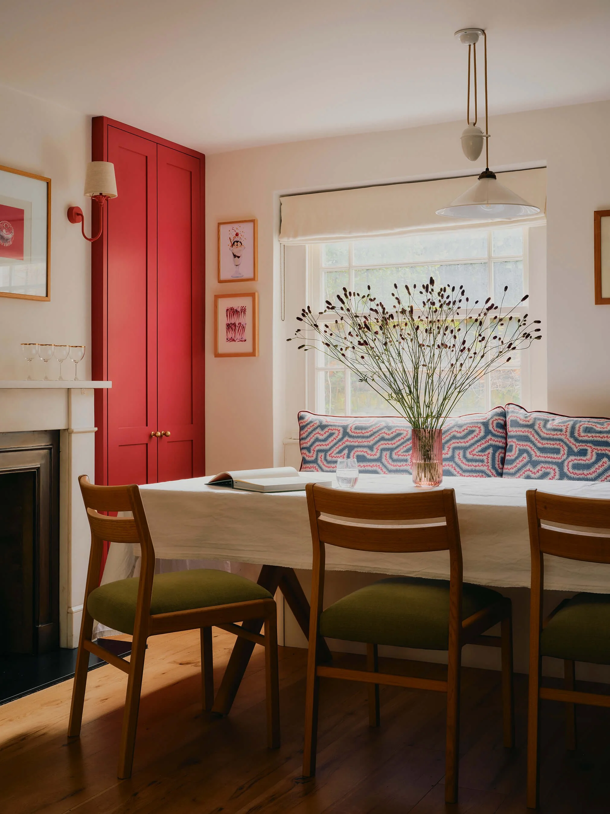 Bright dining space, with table and green chairs and bench. Flowers on top of table, linen tablecloth.