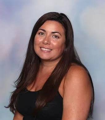 A woman with long dark hair wearing a black tank top, smiling against a light blue background.