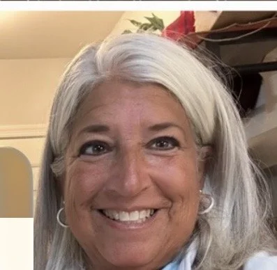 Close-up of a smiling woman with long gray hair and earrings.
