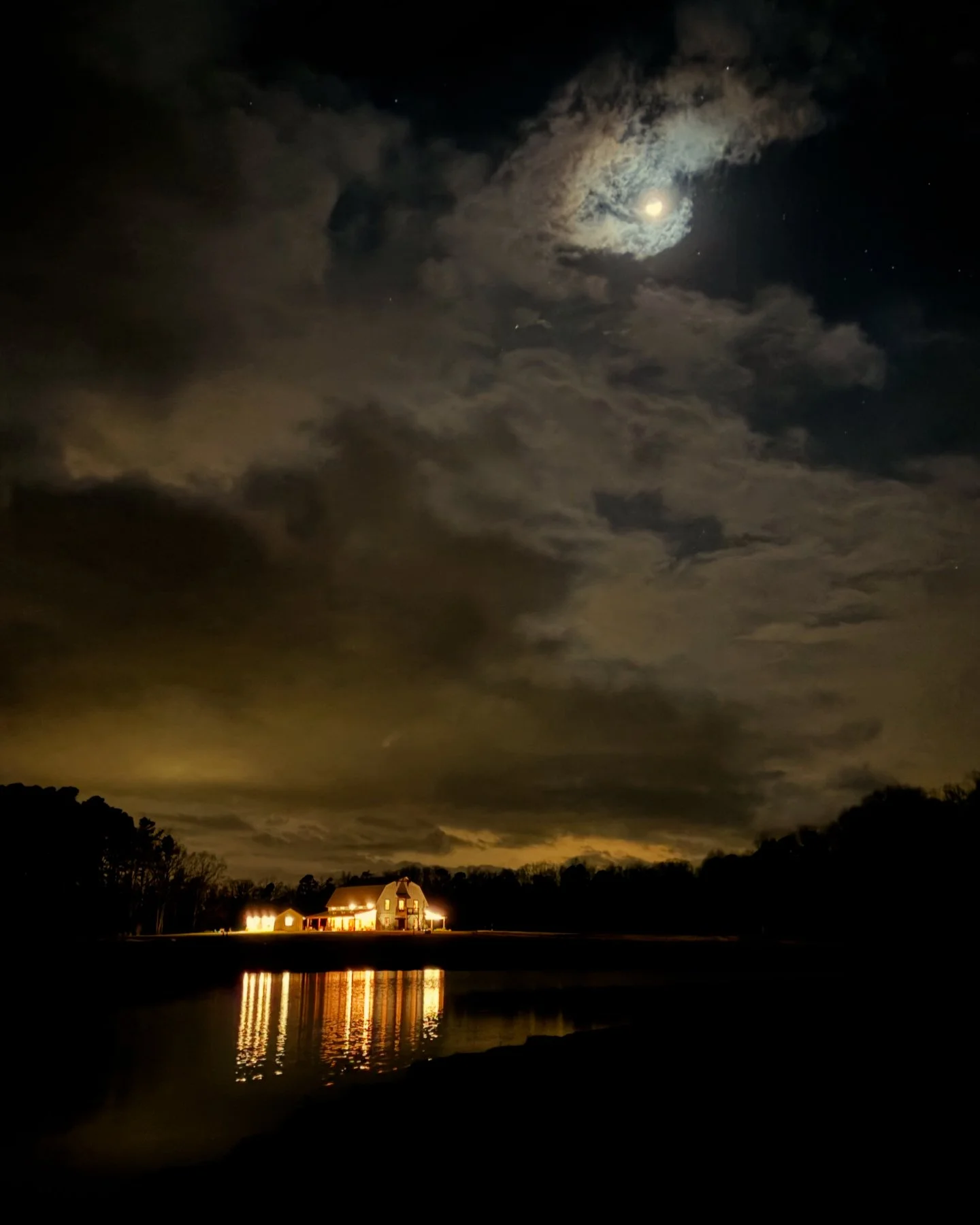 Moonlit night with barn lights reflecting on a pond.