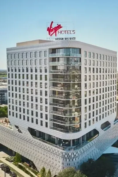 A modern, multi-story Virgin Hotels building with a white exterior, curved glass balconies, and a red Virgin Hotels sign on the roof in the Design District.