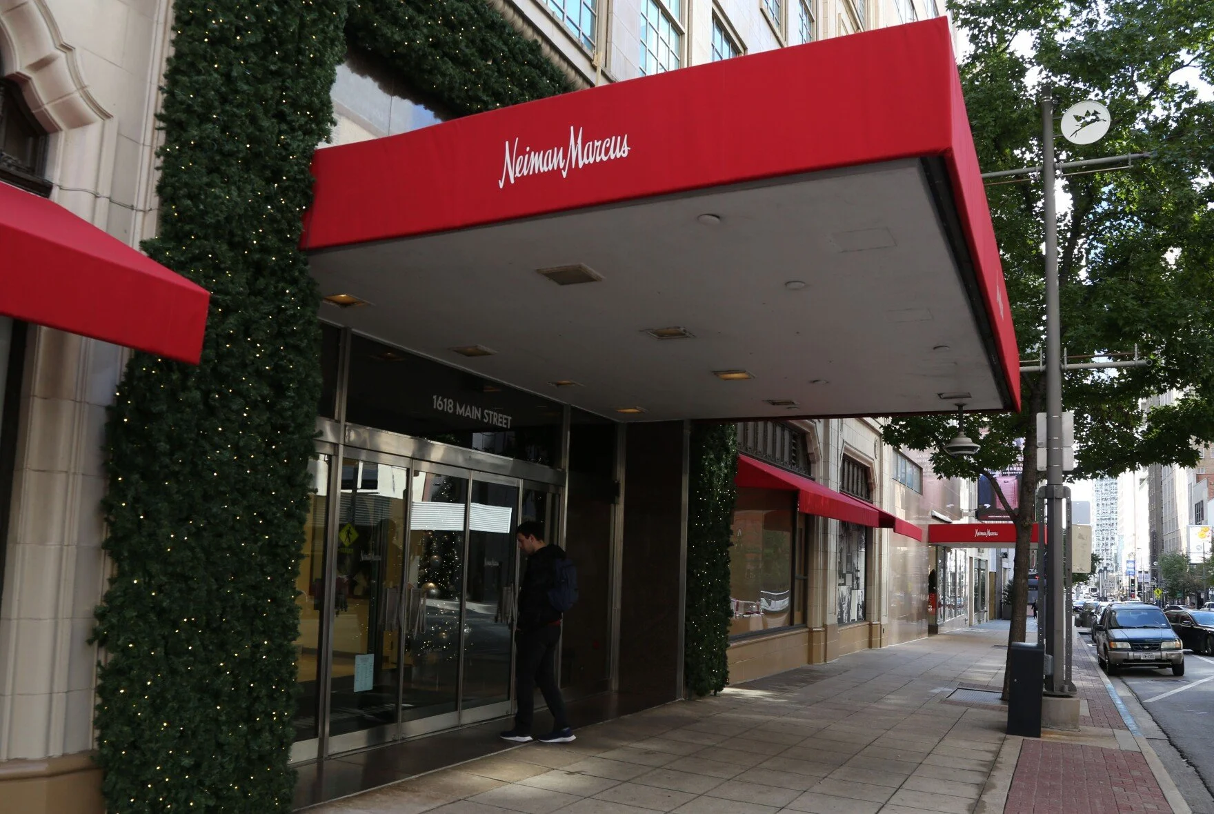 Street view of Neiman Marcus store with red awnings, decorated with Christmas lights, on a city sidewalk with a person entering the store.