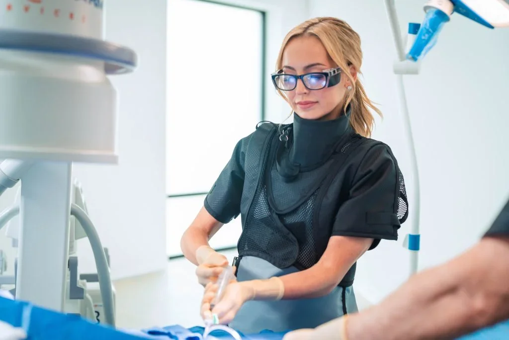 Female dentist in scrubs and glasses performing a dental procedure in a bright dental clinic.