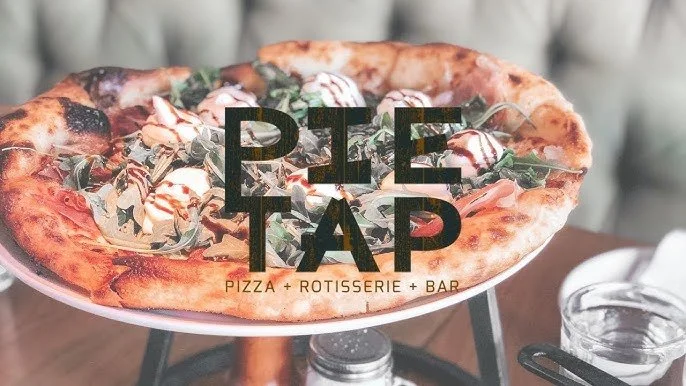 A pizza with seafood, greens, and drizzled sauce on a white platter with the words 'PIZZA + ROTISSERIE + BAR' and an overlay text 'PIE TAP'.