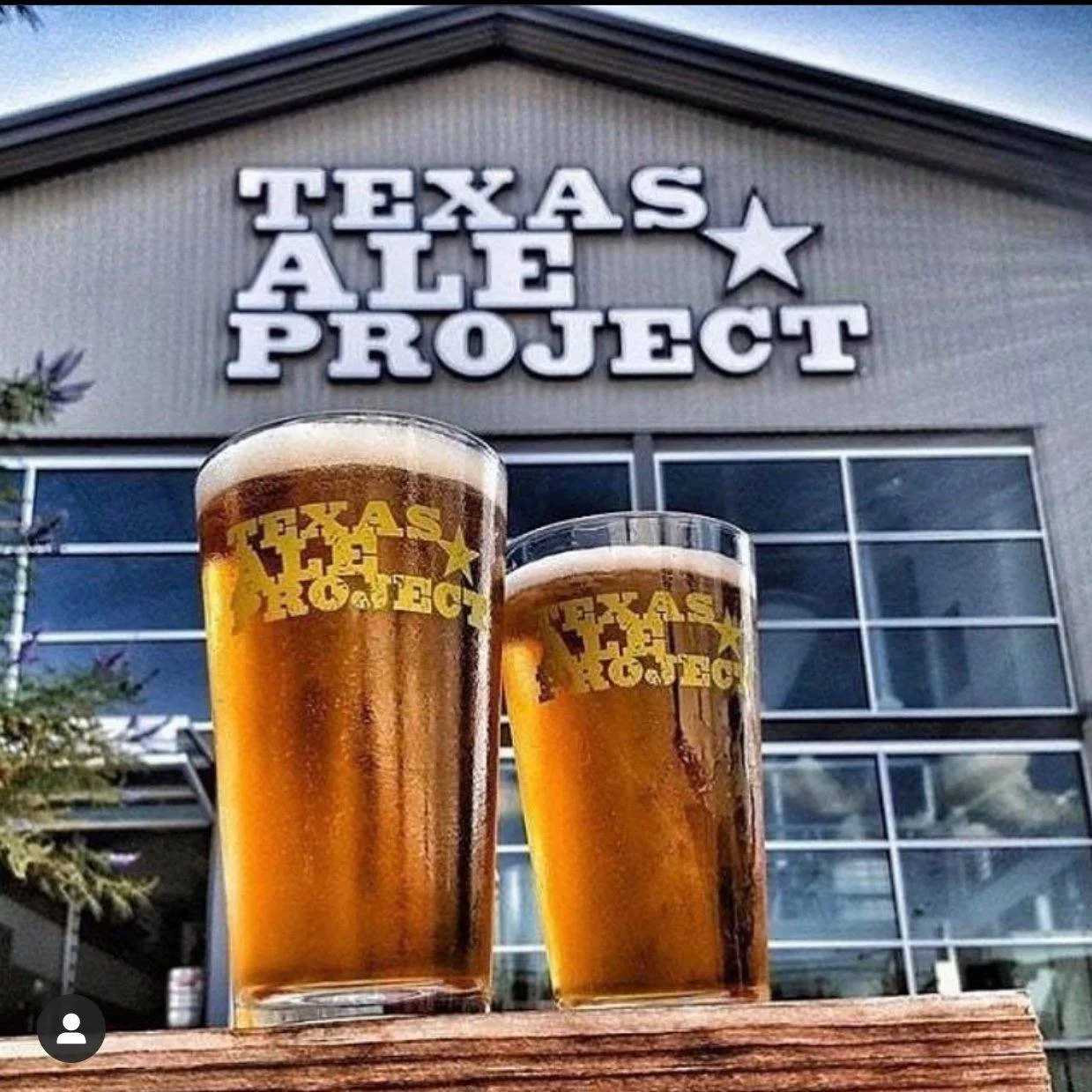 Two glasses of beer with the Texas Ale Project logo in front of the Texas Ale Project building.