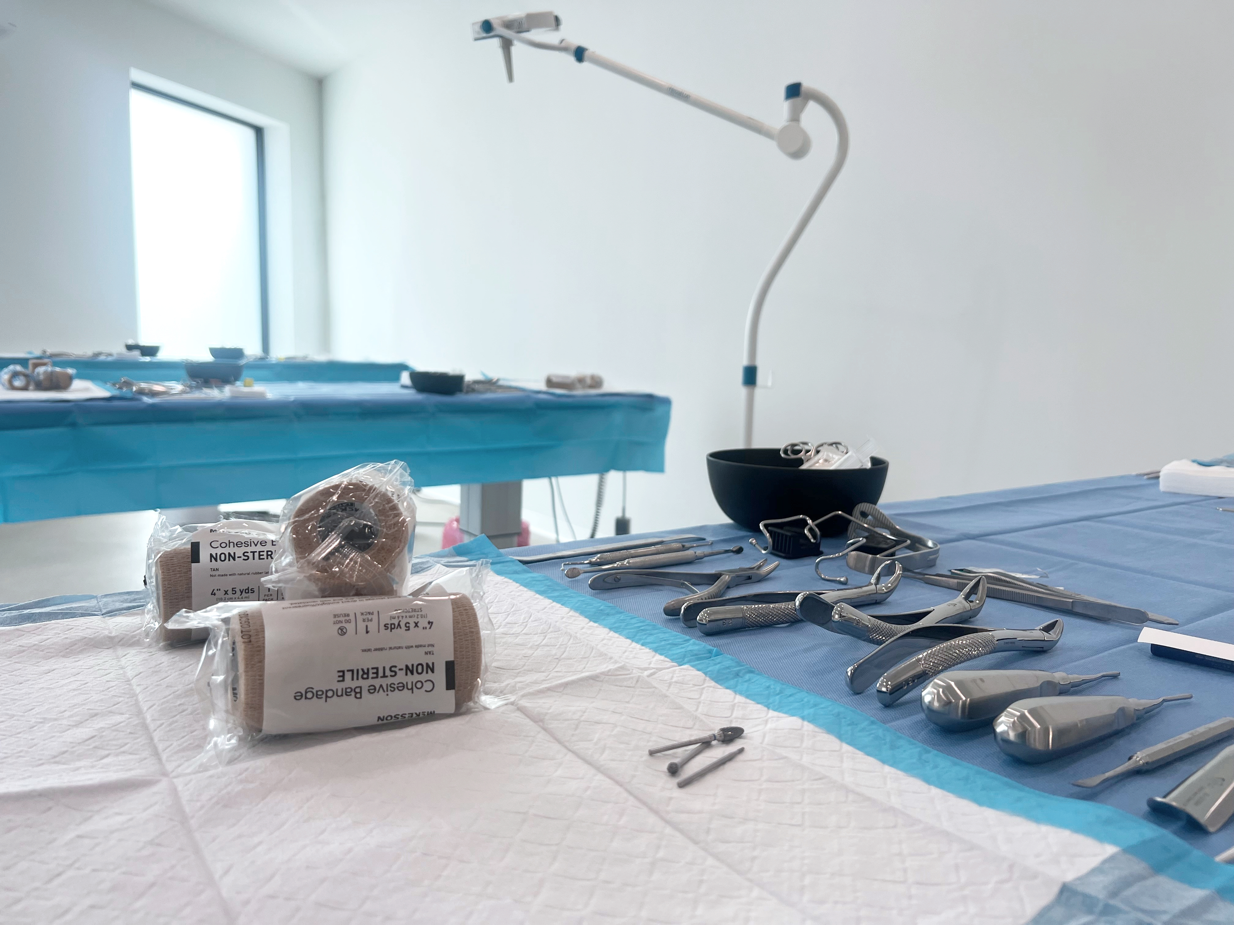 A surgical setup with dental tools, gauze, and sterile supplies on a hospital tray, in a bright operating room.