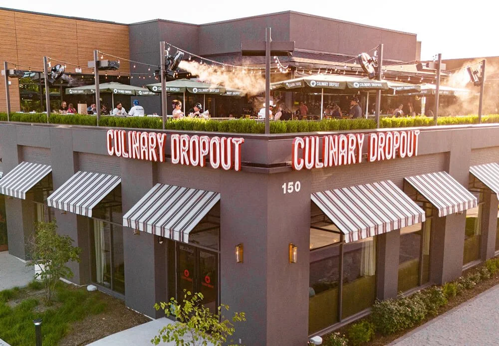 Exterior of a two-story restaurant named Culinary Dropout with outdoor rooftop seating, striped awnings, and a sign displaying the restaurant's name.