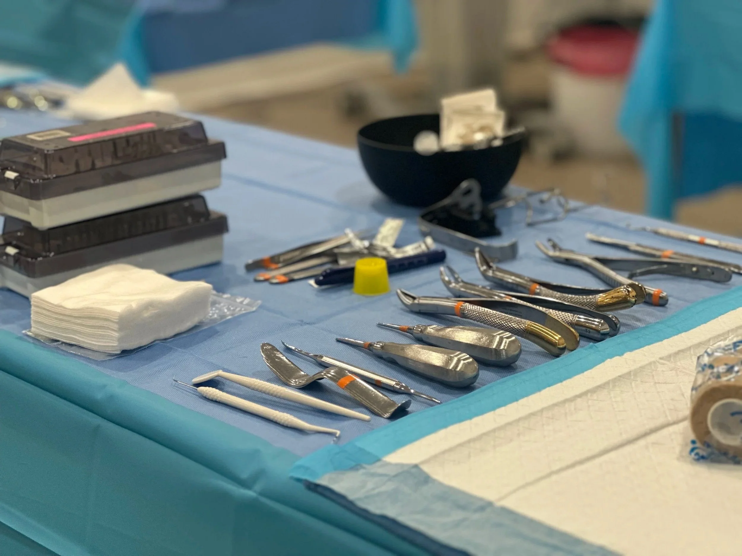 Dental tools arranged on a blue sterile drape, including probes, mirrors, forceps, and cotton rolls, in a dental office setting.