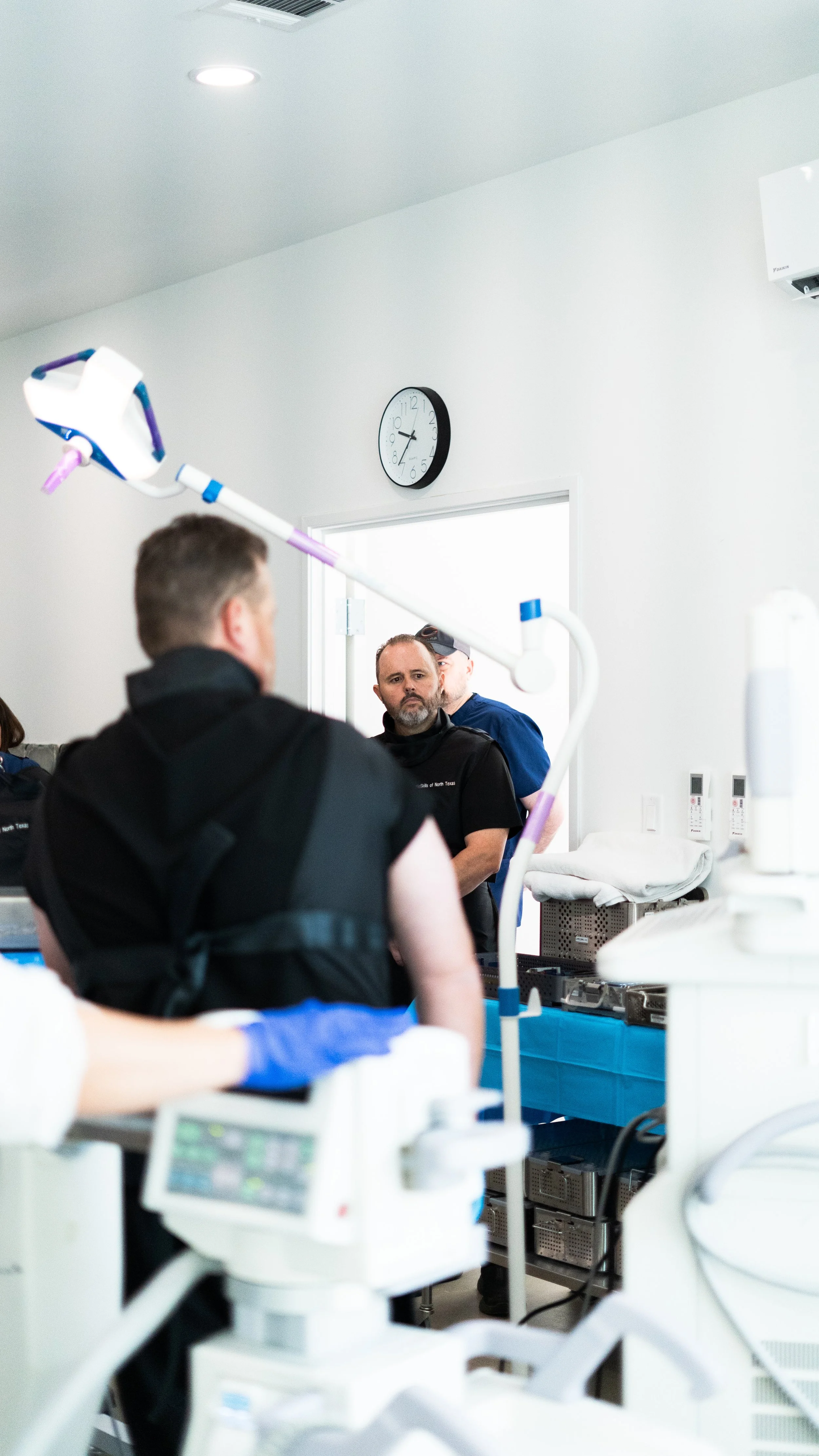 Medical team attending to a patient in an operating room, with medical equipment and monitors visible, and a wall clock showing 12:41.