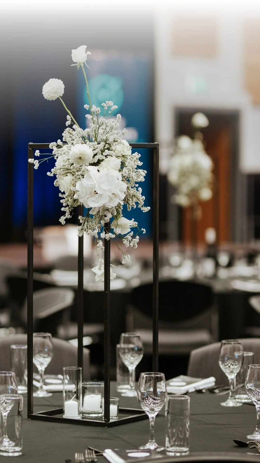 A tall black metal structure with white flowers and candles as table centerpiece at a formal event.