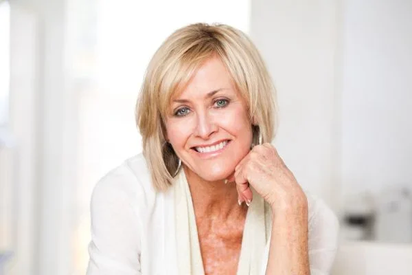 Blond woman in her 50's wearing a pink sweater, smiling and looking directly at the camera.