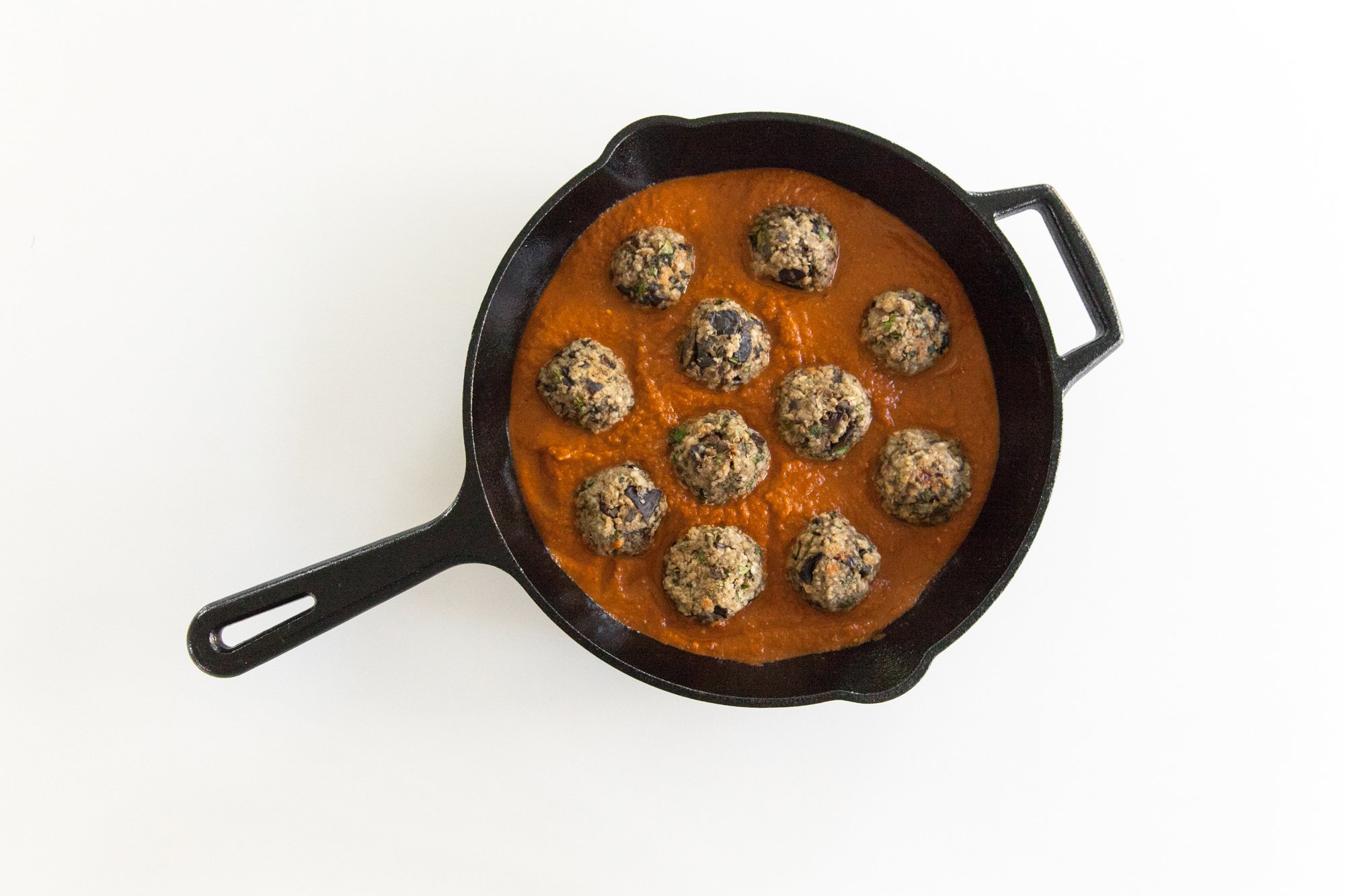  Vegan Eggplant Meatballs in cast iron pan with sauce on white background 