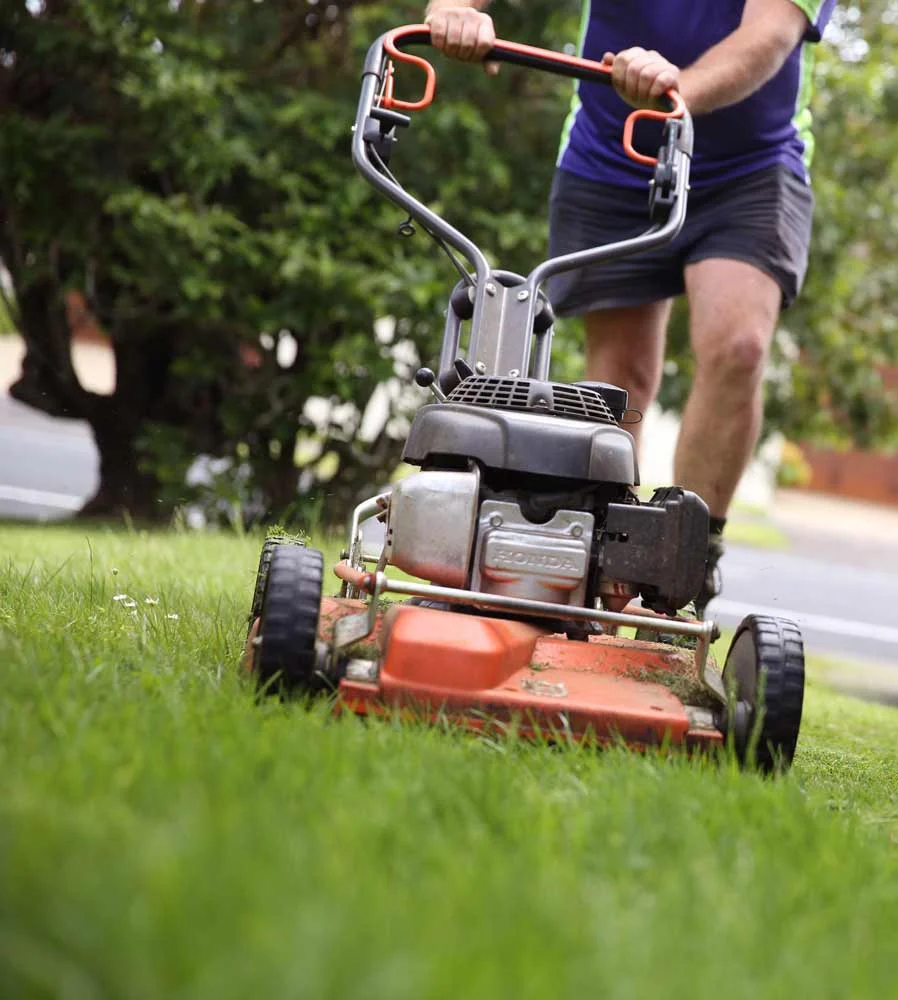 Crewcut operator pushing a lawn mower in grass