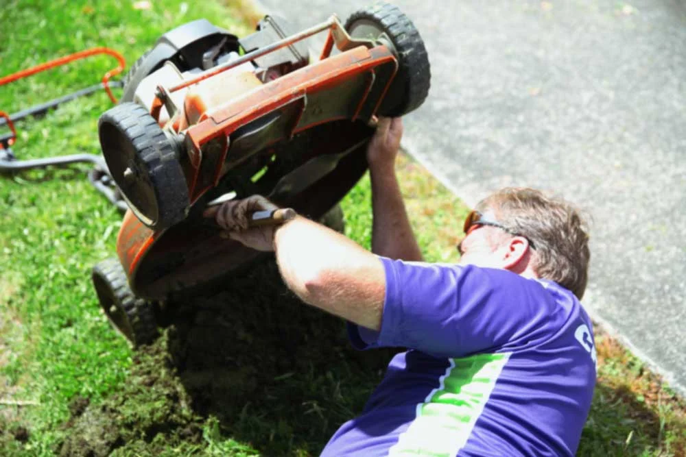 Crewcut business owner maintaining his lawn mower