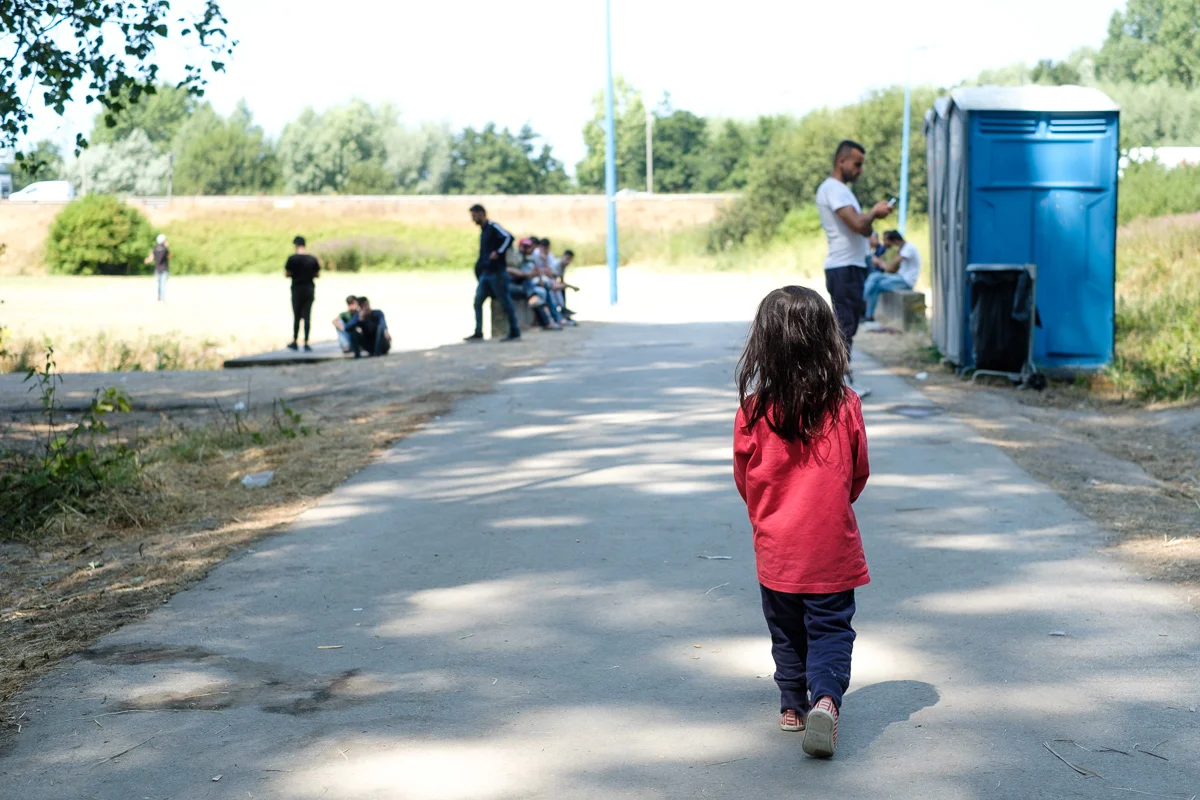 A small migrant girl on her way to the three toilets that have to serve a couple of hundred refugees.