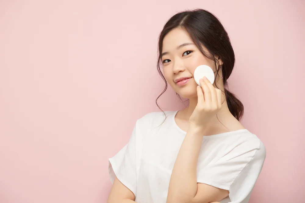 Woman using toner on cotton round.
