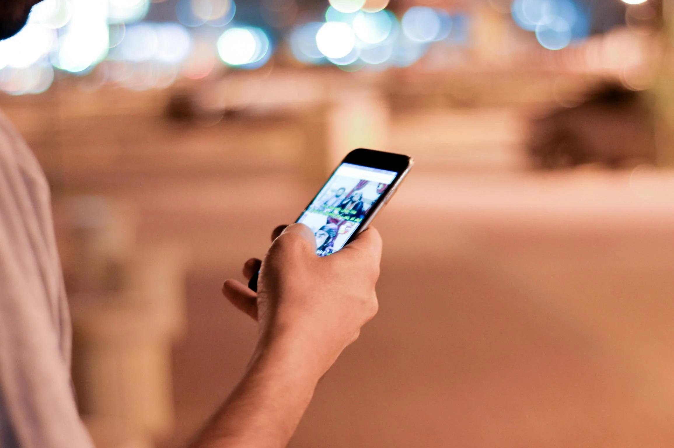 A hand holding a phone at night, city lights blurred in the background